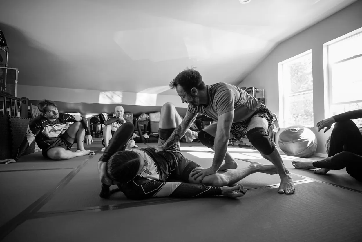 An instructor demonstrating a grappling technique to students on the mats